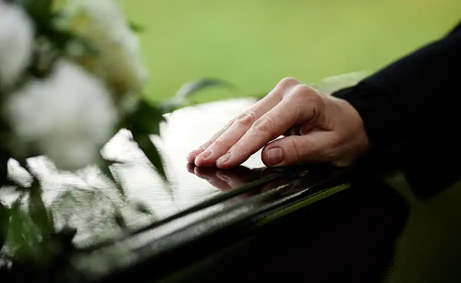 Nahaufnahme einer Frauenhand auf einem Sarg, die sich bei einer Beerdigungszeremonie im Freien verabschiedet. 